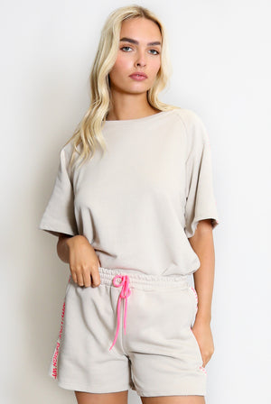 Woman wearing a beige outfit with shorts and a top, standing against a plain background